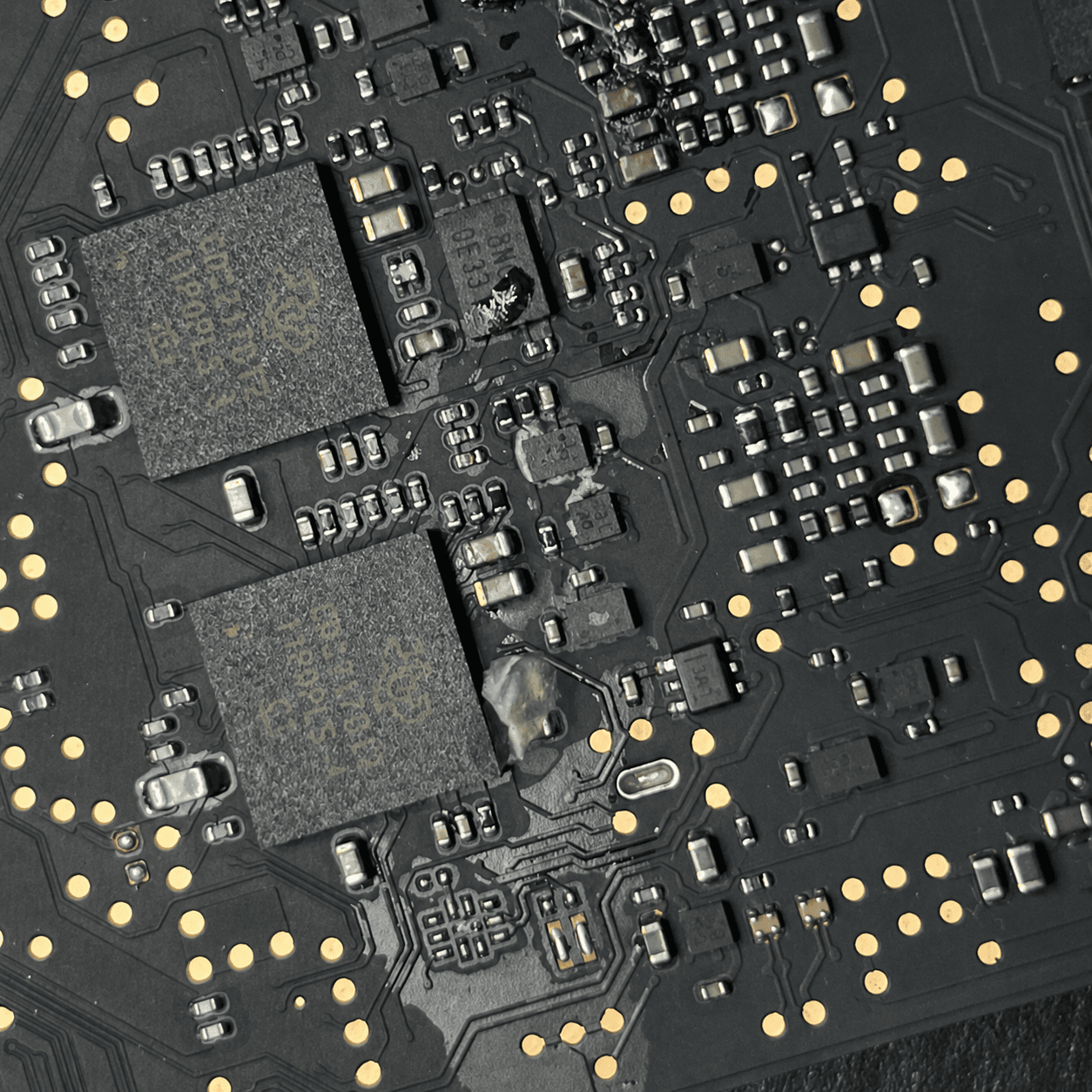 Close-up under magnification of flux and corrosion residue around the NAND flash storage packages on a MacBook A2442 logic board after water exposure
