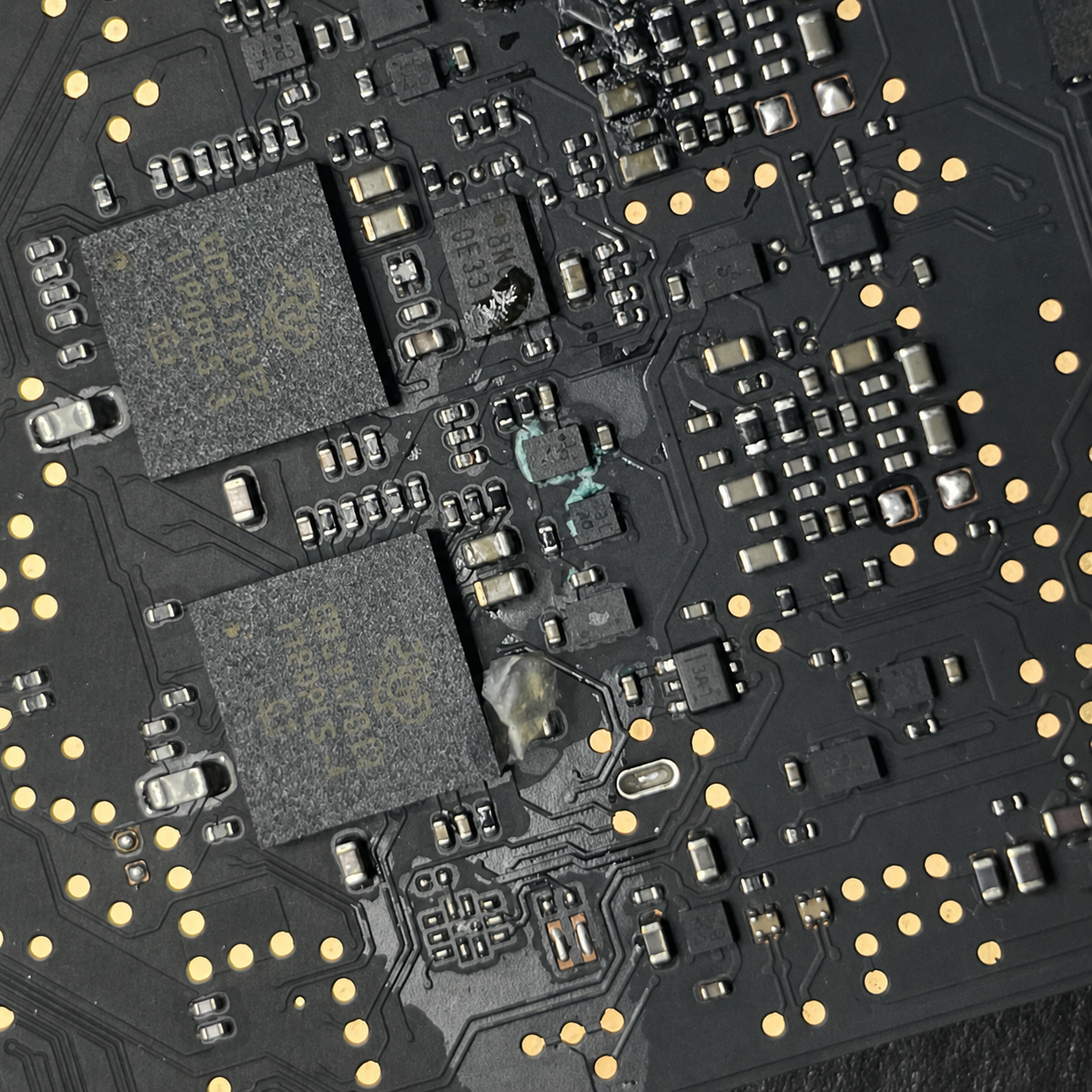 Close-up under magnification of flux and corrosion residue around the NAND flash storage packages on a MacBook A2442 logic board after water exposure